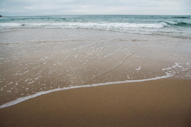 Ondas do mar em uma praia de areia com céu nublado