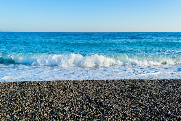 Ondas do mar quebrando em uma praia pedregosa, formando borrifos e respingos