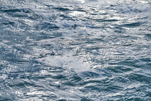 Ondas espumantes escuras do mar tempestuoso, fundo. Aumento da maré ondas azuis escuras frias com espuma do mar em dia nublado.