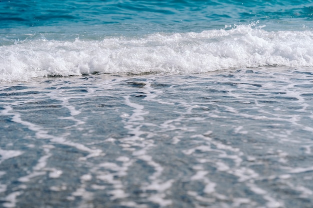 Ondas espumosas brancas na praia de areia closeup. à beira-mar em um dia ensolarado de verão.