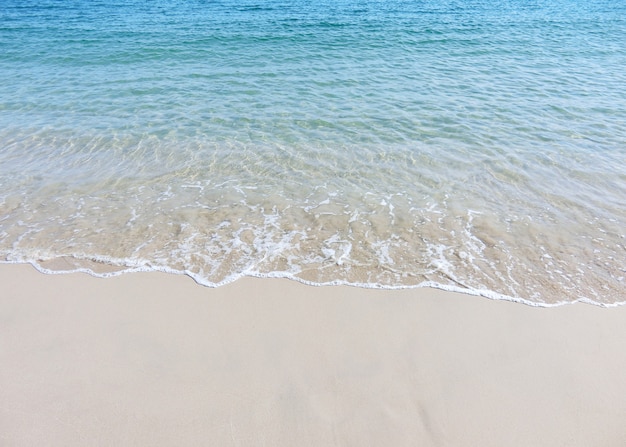 Ondas espumosas em uma praia de areia com água do mar azul em uma praia tropical