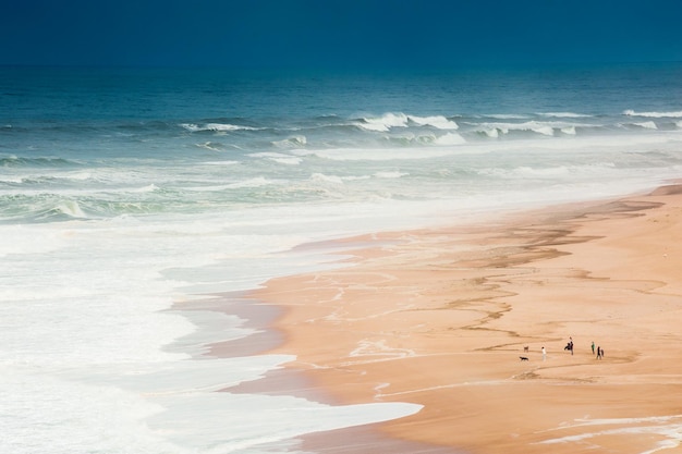 Ondas na costa do Oceano Atlântico, no Algarve, Portugal. Peolpe caminhando na areia da praia