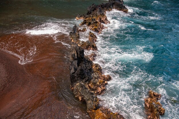 Ondas oceânicas batendo na costa rochosa da ilha Espirrando ondas oceânicas e pedras Red Sand Beach Maui em havaiano