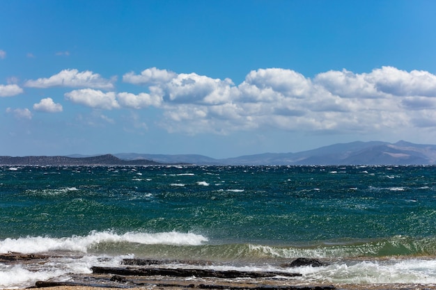 Ondas tempestuosas do mar espirrando no céu azul das rochas com fundo das nuvens