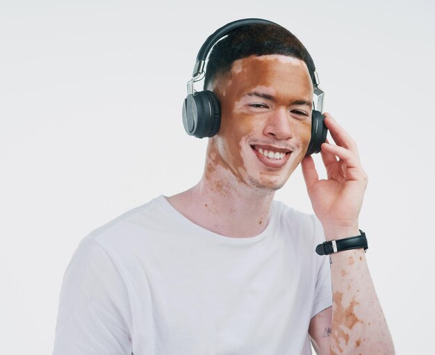 Onde as palavras falham, a música fala Retrato de um jovem bonito com vitiligo ouvindo música com fone de ouvido sem fio em um fundo branco