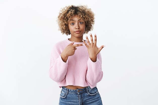 Onde está o meu anel. namorada fofa chateada e irritada esperando por proposta indicando no dedo e perguntando ao namorado sobre casamento ficar descontente esperando muito tempo, posando sobre uma parede branca