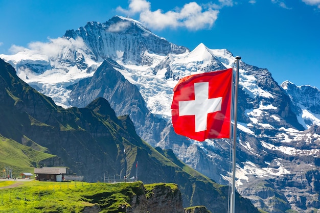 Ondear la bandera suiza y los turistas admiran los picos de la montaña Jungfrau en un mirador de Mannlichen, en el Oberland bernés en Suiza