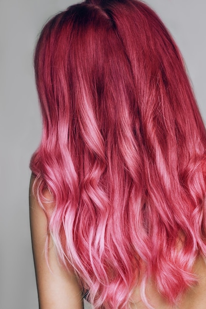 El ondulado cabello rosa intenso de una joven aislada en un fondo gris Resultado de la coloración