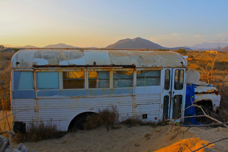 Foto ônibus abandonado no deserto contra um céu claro durante o pôr do sol