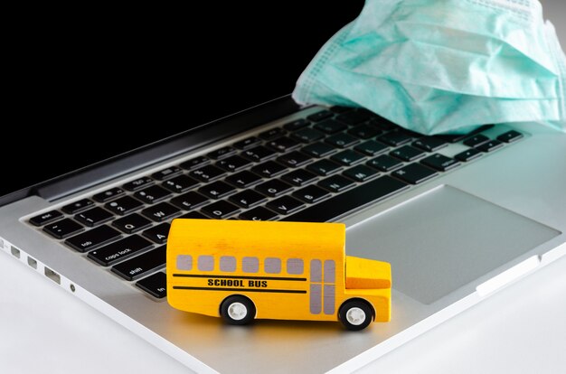 Ônibus escolar amarelo no laptop com máscara facial. educação e conceito on-line durante o período de quarentena