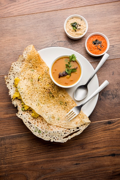 Onion rava masala dosa ist ein südindisches Instant-Frühstück, das mit Chutney und Sambar auf stimmungsvollem Hintergrund serviert wird. selektiver Fokus