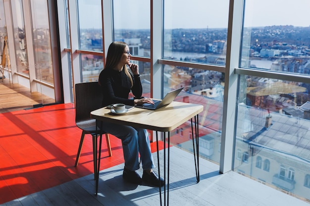 Online-Arbeit in einem Café Fröhliches Mädchen in Freizeitkleidung und Brille mit einem Laptop Fernarbeit oder Bildung mit modernen digitalen Technologien für einen komfortablen Lebensstil in der Stadt