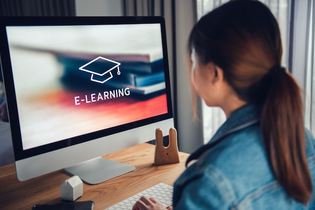 Online-Bildung, E-Learning. Junge Frau sitzt am Tisch und arbeitet am Computermonitor mit Inschrift auf dem Bildschirm