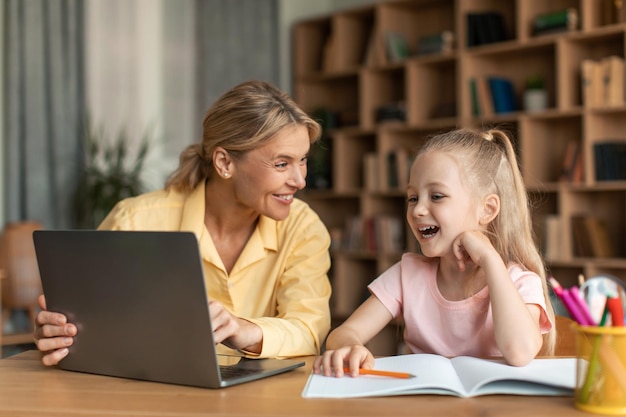 Online-Bildung Glückliche Mutter und ihre kleine Tochter mit Laptop Mutter hilft weiblichem Kind bei den Hausaufgaben