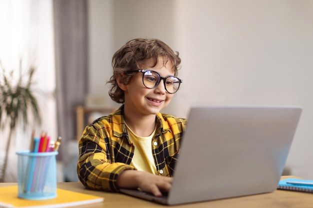 Online-Bildung Porträt eines kleinen cleveren Schülers mit Brille, der zu Hause lernt und Unterricht auf dem Laptop ansieht