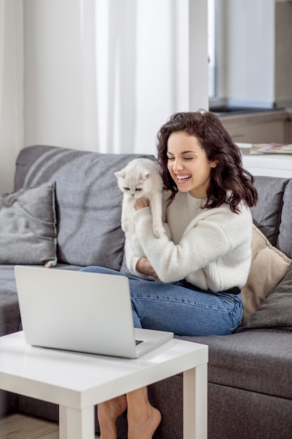 Online. Dunkelhaarige junge Frau umarmt ihre Katze und hat einen Videoanruf