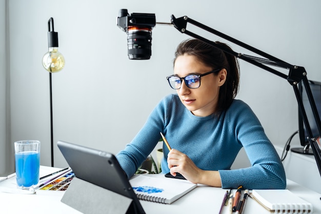 Online-Ersteller von Inhalten vlogger. Eine junge Bloggerin mit Brille entfernt den Inhalt für den Blog, Schulungen. Das Konzept des Online-Lernens, um auf Walercolor zu zeichnen