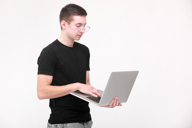 Online-Fernunterricht. Porträt eines jungen Mannes in einem schwarzen T-Shirt mit Brille mit einem Laptop auf einem weißen Hintergrund. Speicherplatz kopieren.