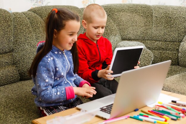 Foto online-fernunterricht. schuljunge und -mädchen, die zu hause mit laptop-notizbuch lernen und hausaufgaben machen. an einem tisch sitzen