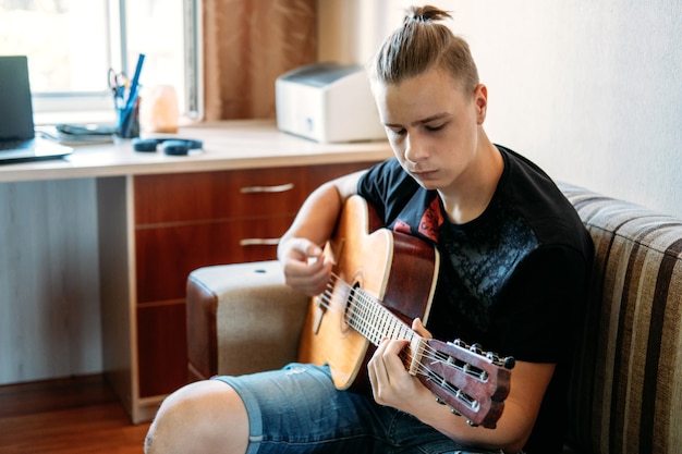 Online-Gitarrenunterricht. Kaukasischer Teenager, der Gitarre spielt, Online-Gitarrenunterricht hat, Lieblingshobby, Freizeit genießt. Wie wählt man eine Gitarre für einen Teenager aus? Akustikgitarren für Anfänger.