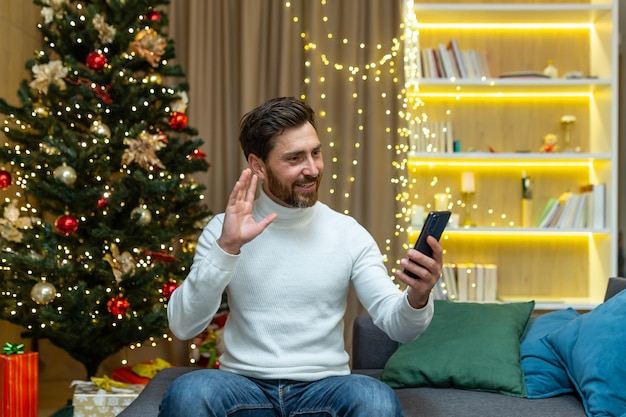 Online-Grüße mit Neujahrsferien junger gutaussehender Mann zu Hause auf dem Sofa, der auf einem Video spricht