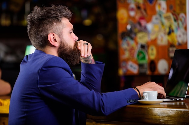 Online-Job Hipster-Freiberufler arbeiten Online-Blog-Notizbuch Surfen im Internet Freiberuflicher Nutzen Mann mit Bart Geschäftsmann sitzt in der Kneipe mit Laptop und einer Tasse Kaffee Manager arbeitet online, während er Kaffee genießt