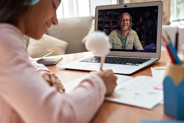 Online-Lehrer-Fernlehrer auf Laptop-Bildschirm, der Fernunterricht für Schülerinnen gibt, die Kopfhörer tragen und zu Hause per Videokonferenz virtuelle Bildung über die Schulter lernen