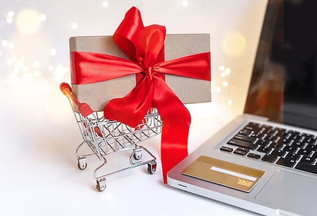 Online-Shopping in den Ferien. Schönes Geschenk zu Weihnachten im Einkaufswagen im Internet gekauft. Online speichern, mit einem Laptop und einer Kreditkarte, Weihnachts-Online-Konzept