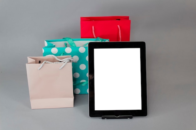 Online-Shopping-Konzept. Nahaufnahme-Tablettenmodell mit weißem Bildschirm mit hellen Geschenktüten auf grauem Hintergrund.