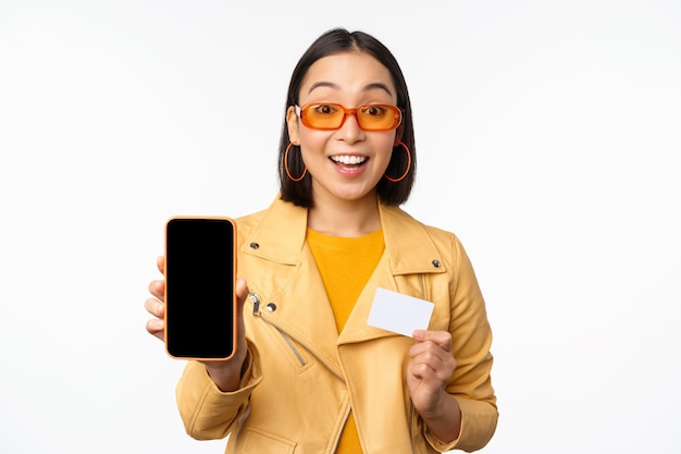 Online-Shopping und People-Konzept Stilvolle asiatische Frau mit Handy-Bildschirm und Kreditkarten-Smartphone-Anwendung auf weißem Hintergrund