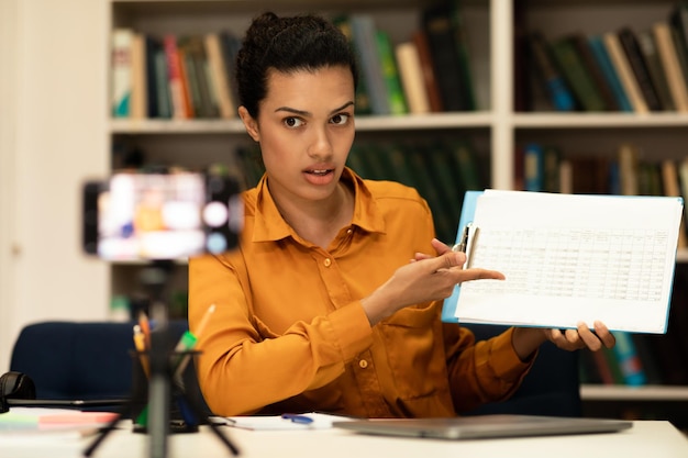 Online-Studium einer jungen Lehrerin, die Unterricht im Internet mit Smartphone auf Stativ gibt und mit spricht