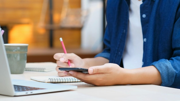 Online-studium mannhandschrift auf notebook während der verwendung des mobiltelefons für den digitalen heimunterricht