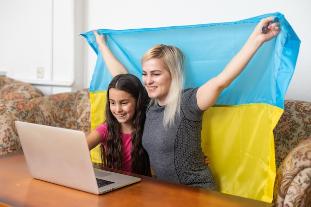 Online-Support für digitale Medien für die Ukraine. Freiheit und Patriotismus-Konzept. mutter und tochter mit laptop und ukraine-flagge