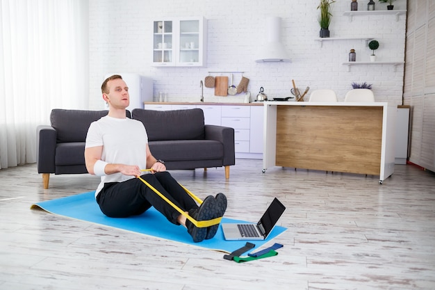 Onlinetraining. junger mann macht übungen mit fitness-gummibändern mit online-tutorial zu hause, freier speicherplatz. sport zu hause machen