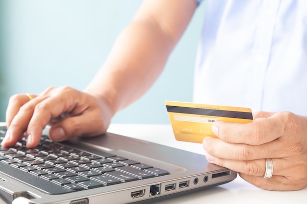 Onlinezahlung, Mannes Hände, die eine Kreditkarte halten und Laptop für das on-line-Einkaufen verwenden