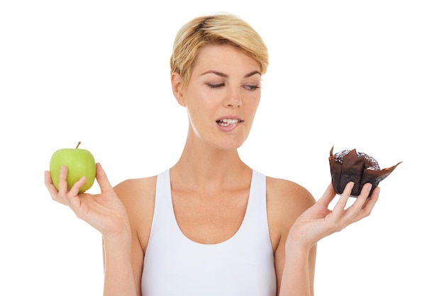 Oooh, no debería, pero es tan tentador Captura recortada de una mujer joven que sostiene una manzana y un dulce que parece indecisoImagen aislada