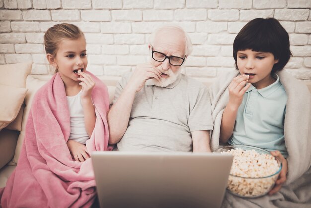 Opa und Kinder schauen sich einen Film an Essen Sie Popcorn.
