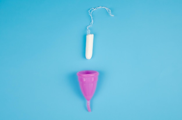 Foto opciones: copa menstrual o tampón. tampón de higiene femenina y copa menstrual sobre un fondo azul. productos de higiene femenina. enfoque selectivo. higiene y ecología