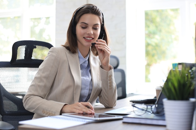 Operador autónomo hablando con auriculares y consultando a clientes desde la oficina.