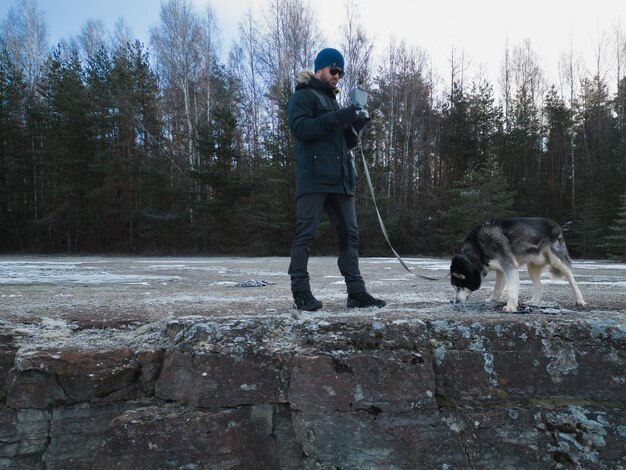 Un operador de avión no tripulado con un panel de control en sus manos con un perro husky en la naturaleza