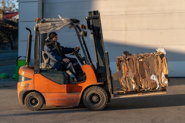 El operador de la carretilla elevadora trabaja en el territorio de la tienda Transporte de mercancías en una carretilla elevadora Planta de reciclaje de papel de carga de papel usado