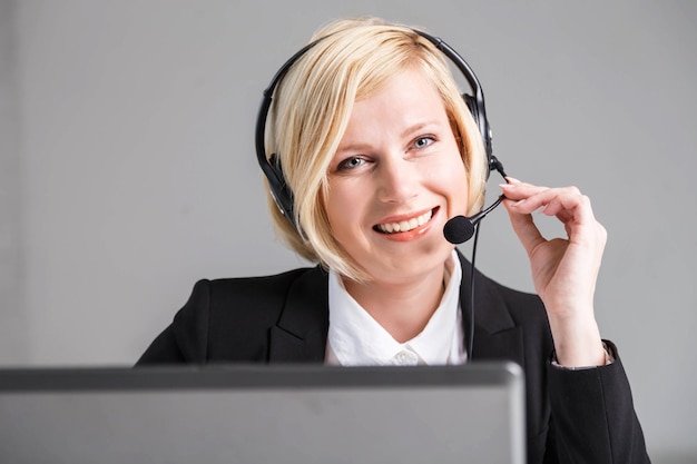 Operador de centro de llamadas de mujer rubia muy sonriente vestida con traje negro elegante con auriculares