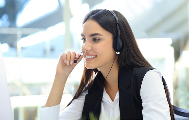 Operador de call center feminino jovem e bonita com fone de ouvido no escritório.