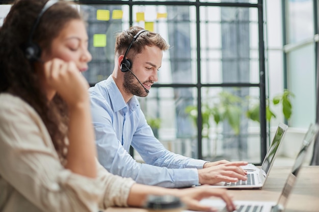 Operador de callcenter masculino com fones de ouvido sentado em um escritório moderno