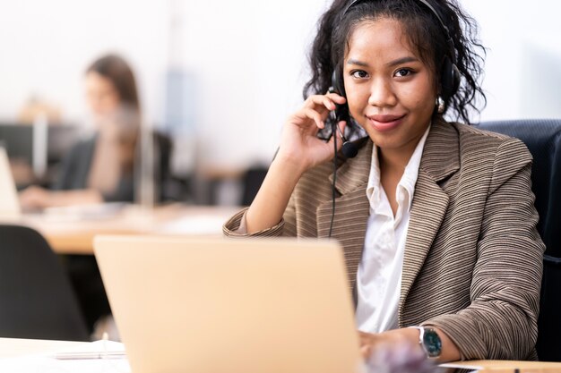 Operador de confiança amigável jovem adulto raça mista de mulher africana e asiática com fones de ouvido trabalhando em uma central de atendimento