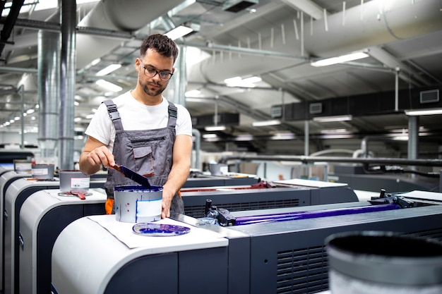 Foto operador de máquina de impressão preparando tinta para processo de impressão na gráfica.