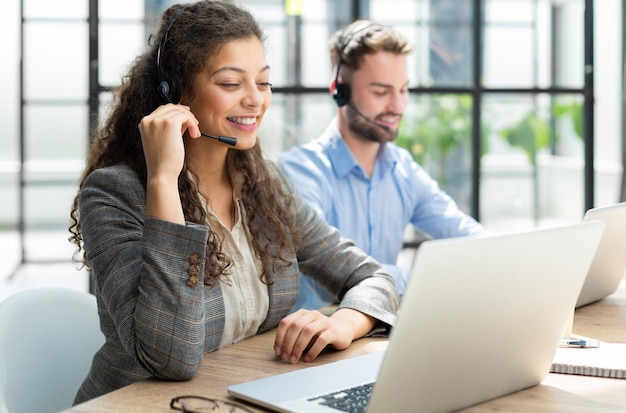 Operador de suporte ao cliente feminino com fone de ouvido e sorrindo com colegas ao fundo