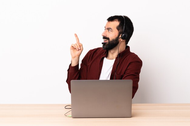 Operador de telemarketing homem caucasiano trabalhando com um fone de ouvido e com o laptop com a intenção de realizar a solução enquanto levanta um dedo