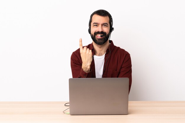 Operador de telemarketing homem caucasiano trabalhando com um fone de ouvido e com o laptop, fazendo o gesto vindo