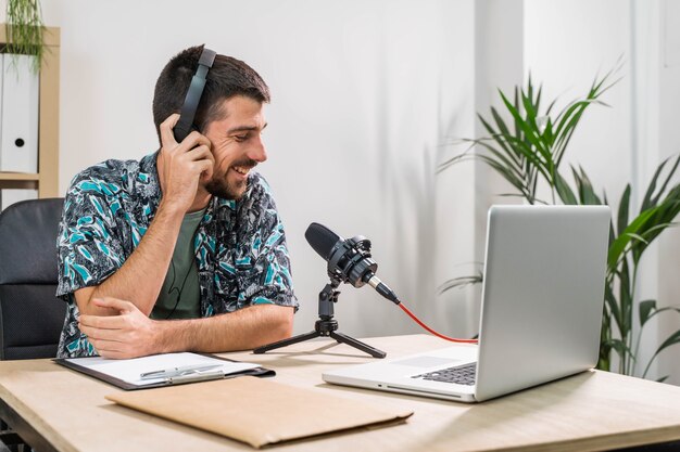 Operador de telemarketing ou podcast trabalhando com um laptop e falando em um fone de ouvido no escritório do estúdio